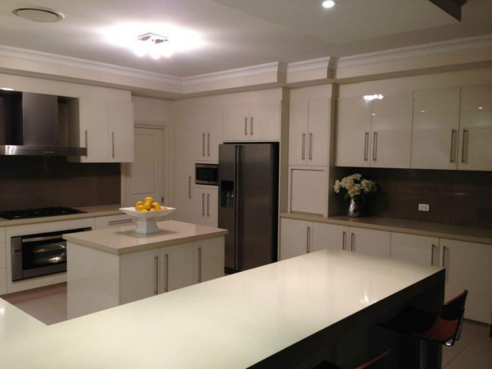 Cream gloss kitchen with an island bench, dark stone splashback and an integrated oven tower