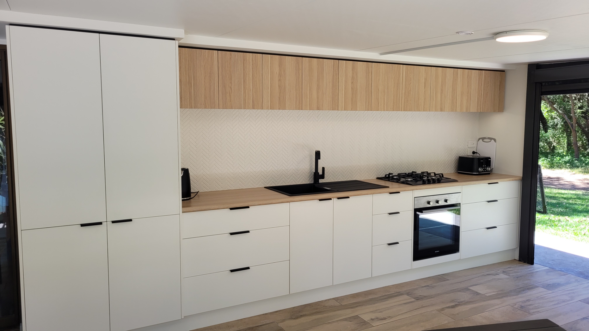 Handleless white cabinetry with oak overhead cupboards and a timber benchtop