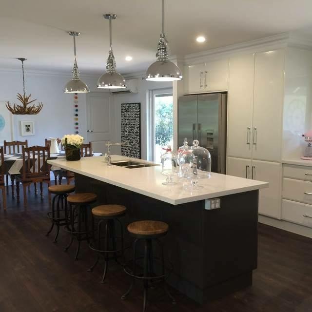 White gloss kitchen with a long dark fronted island, stone waterfall top and chrome pendants