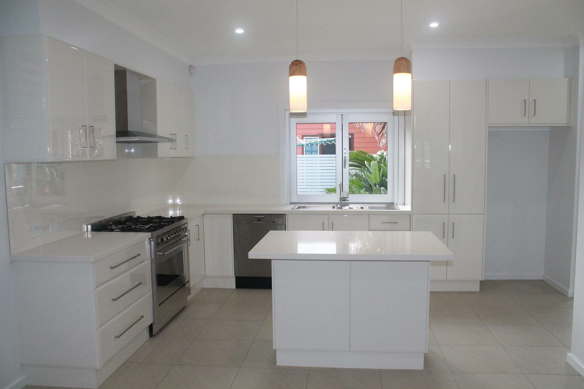 New all white gloss kitchen with an island bench, freestanding oven and floor to ceiling cabinetry