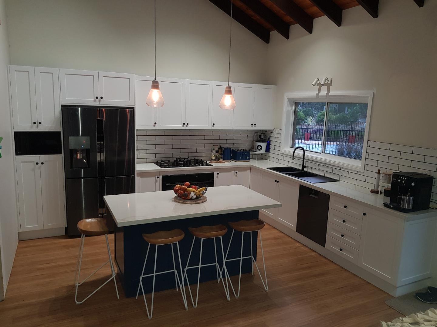 White shaker kitchen with a navy island and exposed timber rafters